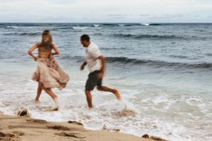 Elopement Photographer, a man and woman run together through the ocean tide