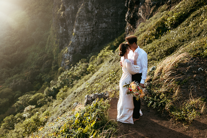 Elopement Photographer, bride in dress stands with groom on lush Hawaiian trails